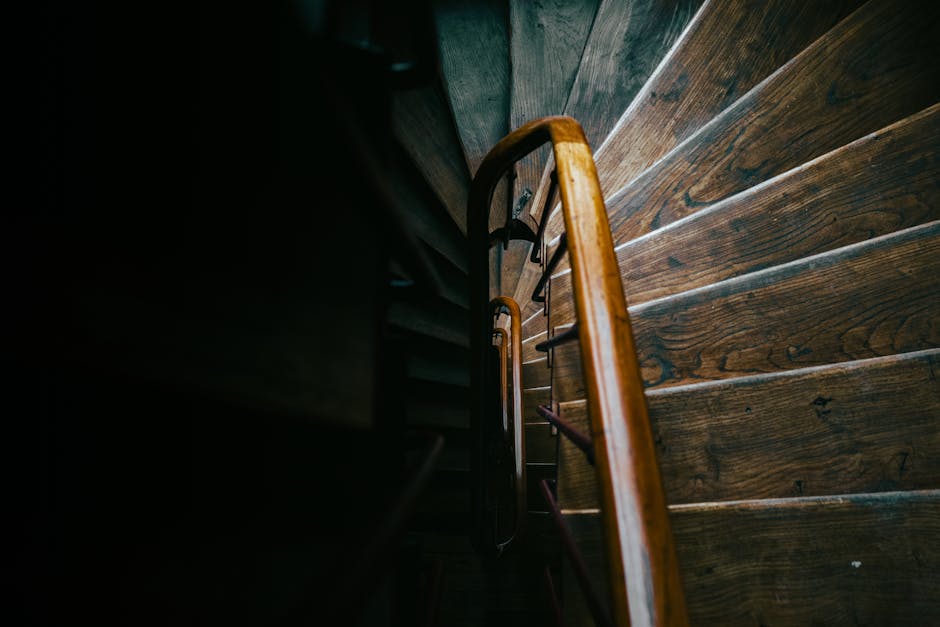 A top-down view of a spiral staircase inside a residential property, featuring white marble steps with grey veining. The staircase has a wrought iron railing with decorative balusters and a polished w