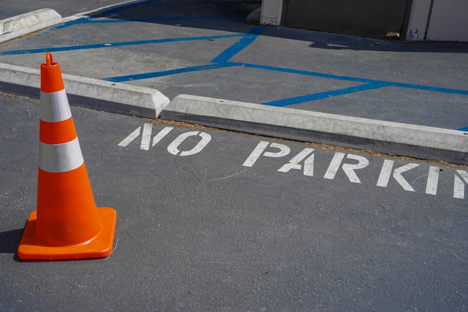 A rectangular white metal sign mounted on a light grey wooden garage door, displaying bold black text that reads 'NO PARKING DAY OR NIGHT'. The sign is attached with four corner screws and is position