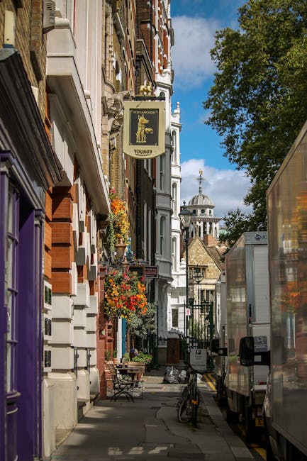 A narrow residential street in Maida Vale featuring a row of Victorian-style terraced houses with white and red brick facades, decorative architectural details, and bay windows. The pavement on the le